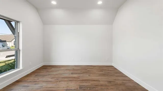 a view of an empty room with wooden floor and a window