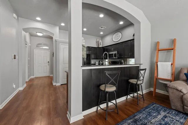 a kitchen with stainless steel appliances granite countertop a refrigerator a sink dishwasher and a dining table with wooden floor