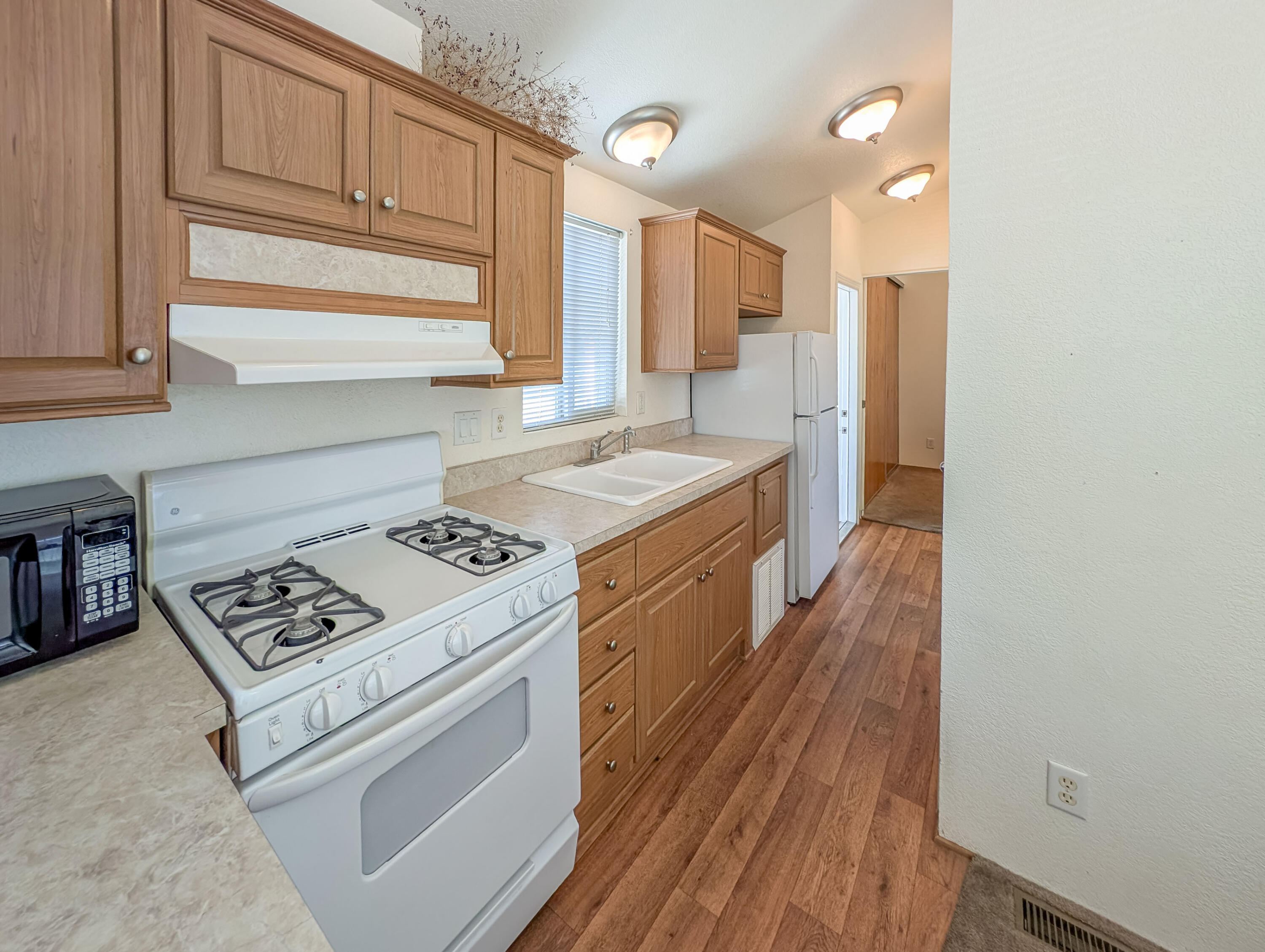 70200 Dillon Road, Unit 169 Desert Hot Springs, CA 92241 - Photo 10 of 25 a kitchen with granite countertop a stove a sink dishwasher and white cabinets with wooden floor
