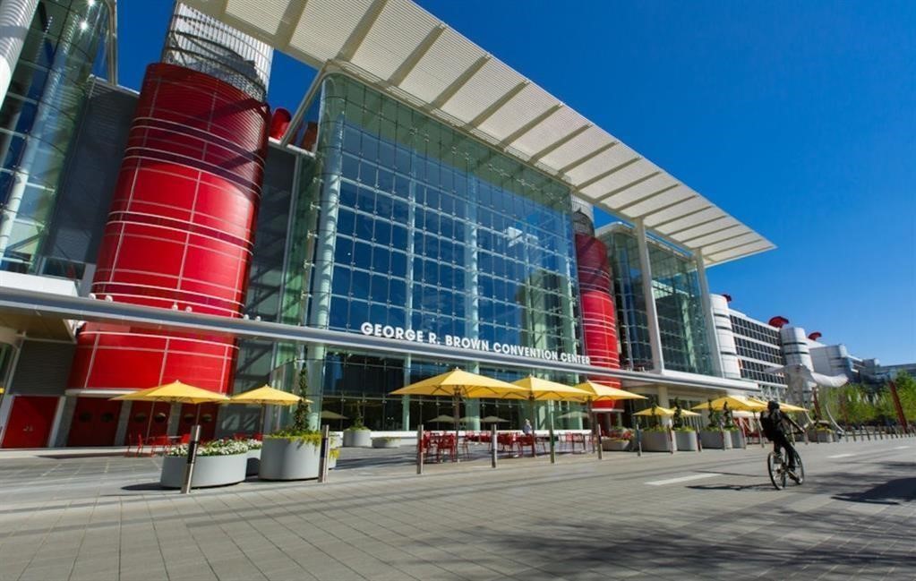 710 Delano Street, Unit A Houston, TX 77003 - Photo 31 of 32 George R. Brown Convention Center with striking red cylindrical structures and expansive glass facades. The area is spacious with wide walkways and outdoor seating under yellow umbrellas, a bustling urban environment nearby.