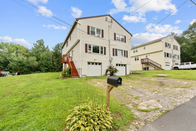 a view of a white house next to a yard with big trees