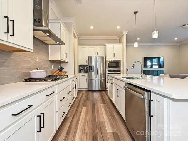 a large kitchen with stainless steel appliances kitchen island granite countertop a stove a sink dishwasher and a refrigerator with wooden floor