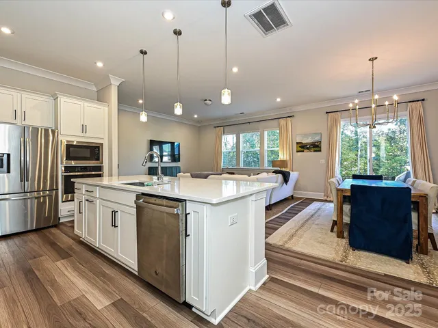 a kitchen with stainless steel appliances granite countertop a refrigerator a sink dishwasher a oven and a dining table with wooden floor