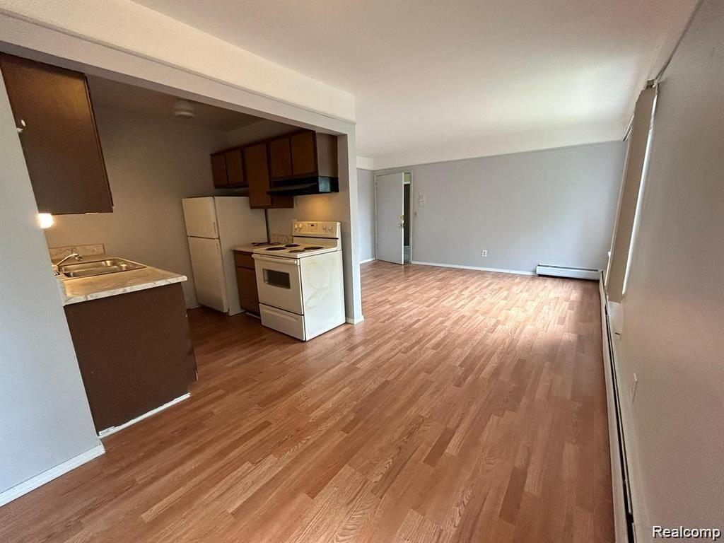 16480 East 9 Mile Road, Unit 102 Eastpointe, MI 48021 - Photo 6 of 13 Wood-finish flooring throughout, kitchen with brown cabinetry and white appliances, and light gray wall paint