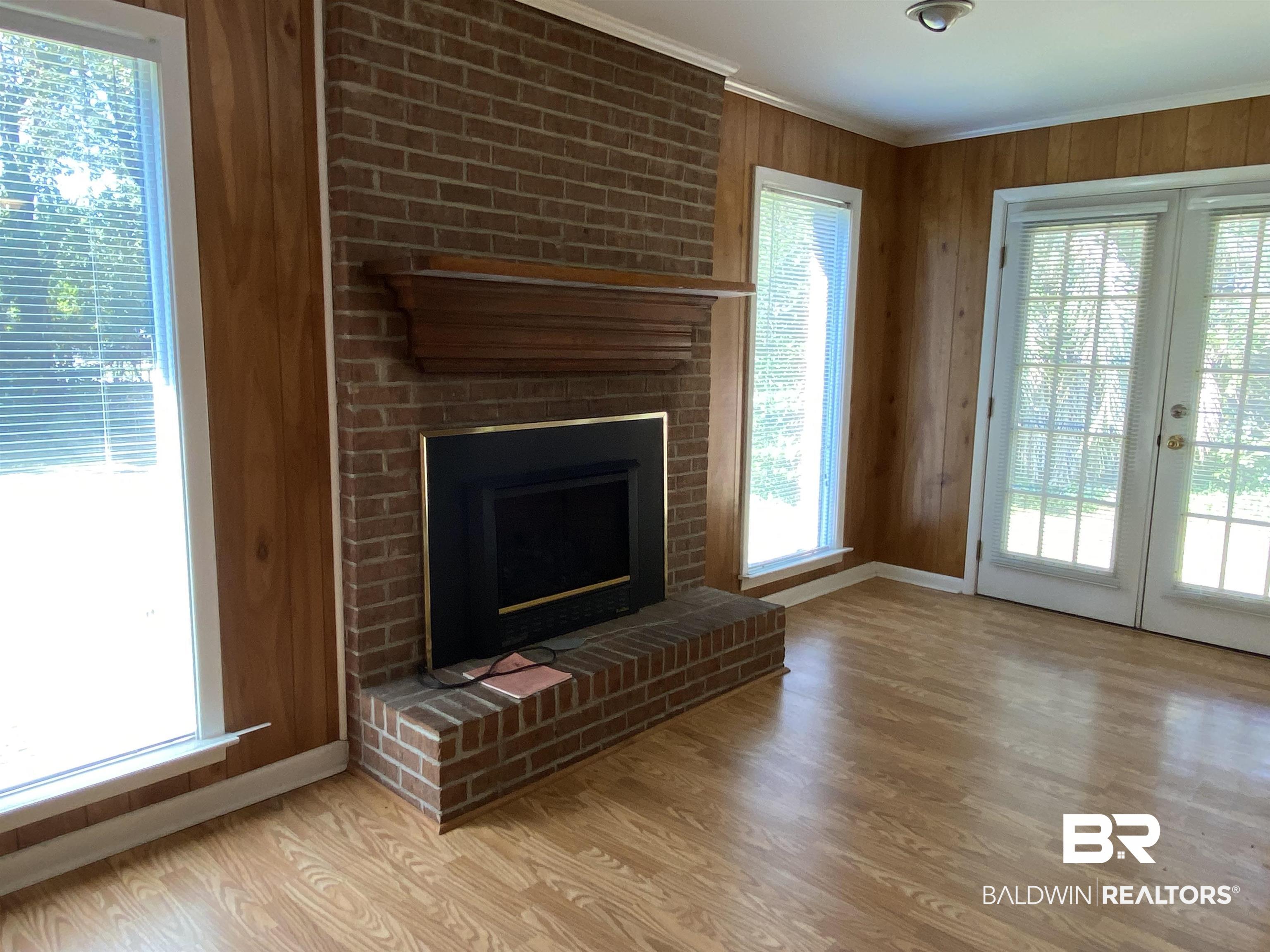106 Terry Drive Brewton, AL 36426 - Photo 11 of 25 Unfurnished Den with wooden walls, light wood finished floors, a fireplace, crown molding, and french doors