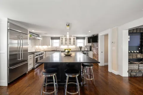 a kitchen with stainless steel appliances granite countertop a dining table chairs refrigerator and sink