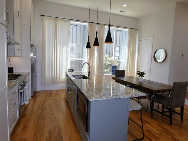 a kitchen with stainless steel appliances granite countertop a table chairs in it and wooden floors