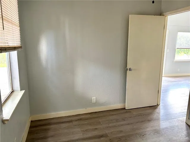 an empty room with wooden floor and windows with curtains