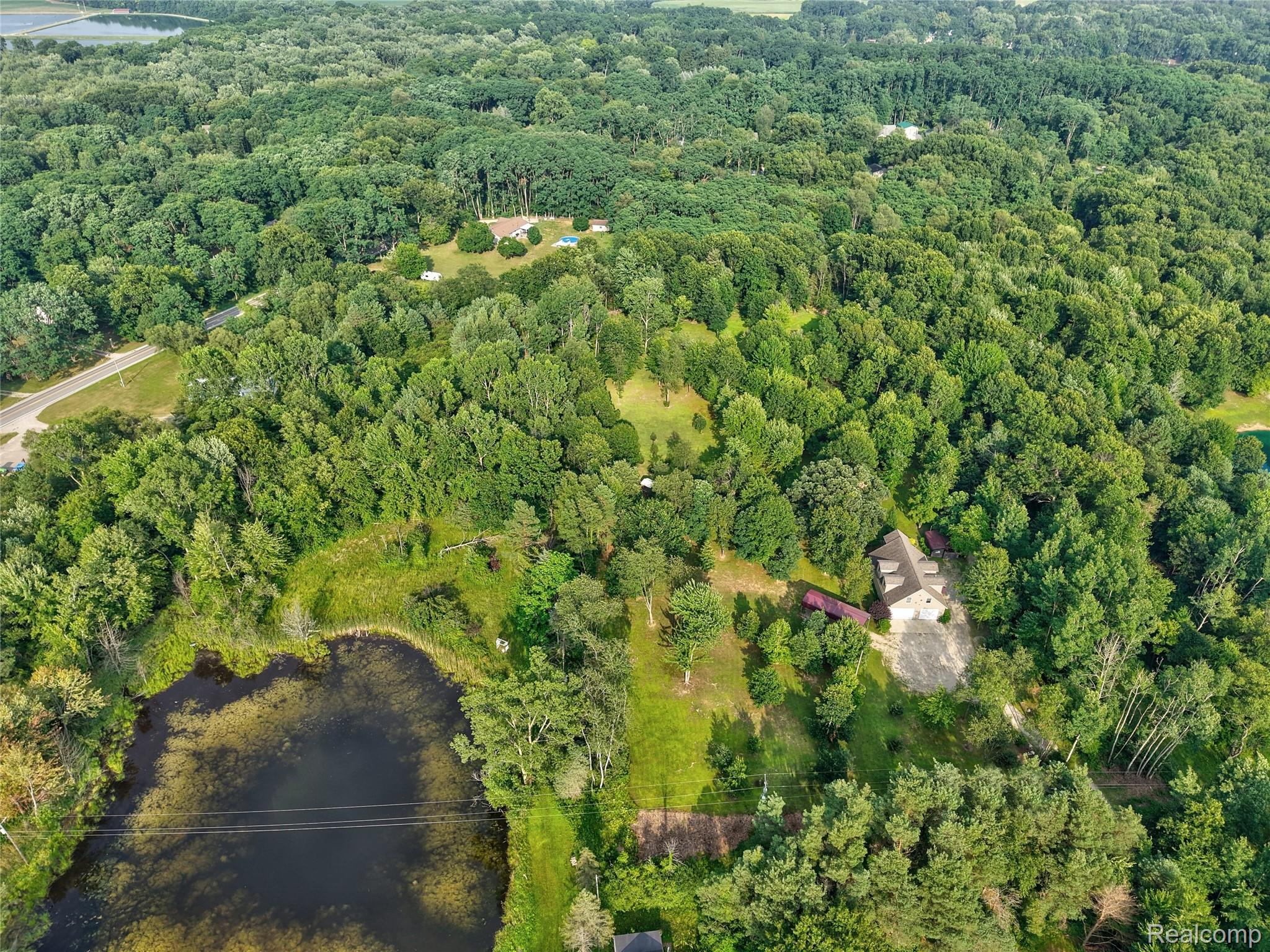 15055 South Duffield Road Byron, MI 48418 - Photo 57 of 61 Expansive wooded property featuring a natural pond, a winding paved road, and a residential structure with an accompanying outbuilding