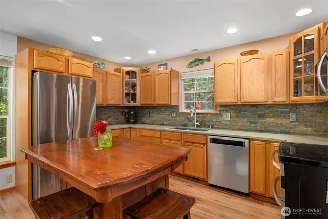 a kitchen with stainless steel appliances granite countertop a refrigerator a sink dishwasher a stove and white countertops with wooden floor