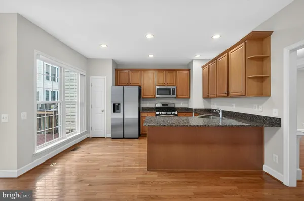 a kitchen with stainless steel appliances granite countertop a refrigerator a stove top oven a sink and dishwasher with wooden floor