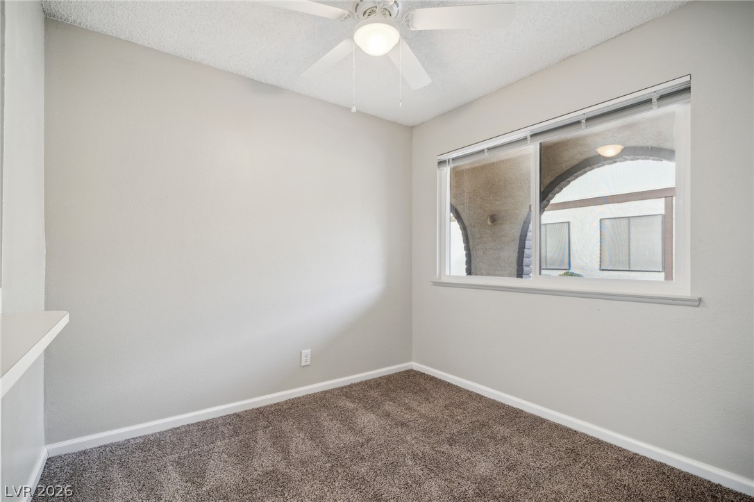 5733 Smoke Ranch Road, Unit D Las Vegas, NV 89108 - Photo 4 of 14 Empty room featuring dark colored carpet, a ceiling fan, and a textured ceiling
