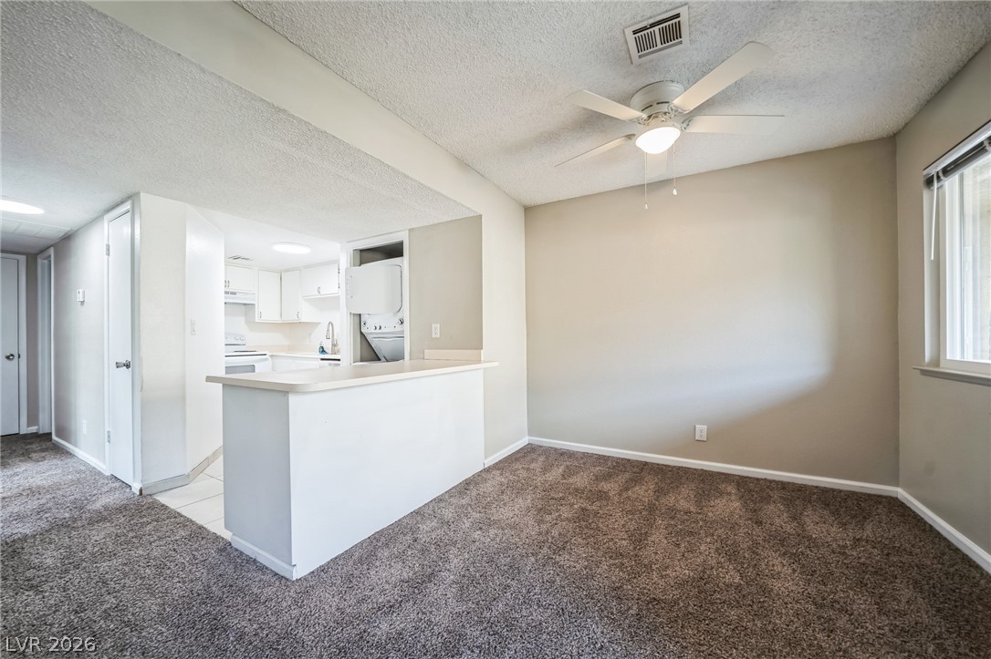 5733 Smoke Ranch Road, Unit D Las Vegas, NV 89108 - Photo 5 of 14 Kitchen featuring light colored carpet, white cabinets, a peninsula, light countertops, and a textured ceiling