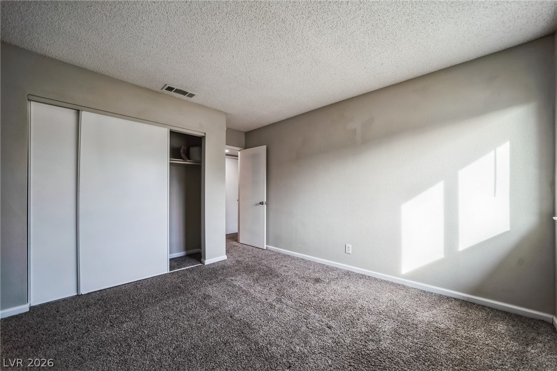 5733 Smoke Ranch Road, Unit D Las Vegas, NV 89108 - Photo 10 of 14 Unfurnished bedroom featuring a textured ceiling, a closet, and dark colored carpet