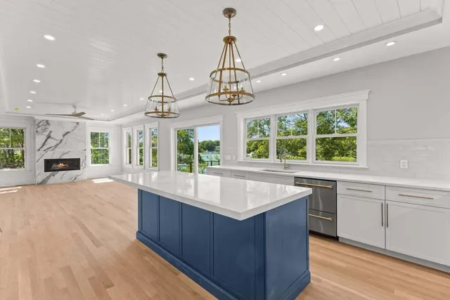 a kitchen with kitchen island granite countertop a stove a sink a counter space wooden floor and windows