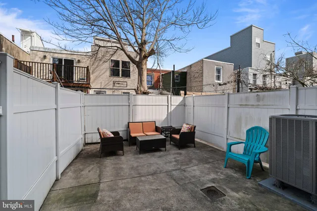 a view of a patio with couches table and chairs under an umbrella with wooden fence