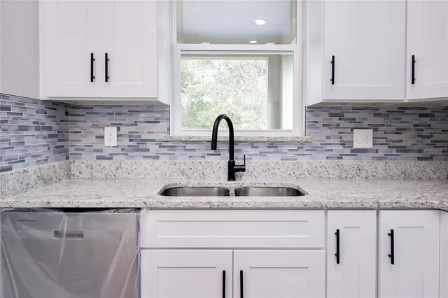 a kitchen with granite countertop a sink white cabinets and a window