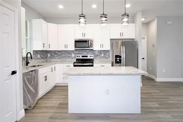 a kitchen with stainless steel appliances a stove top oven a sink a refrigerator white cabinets and wooden floor