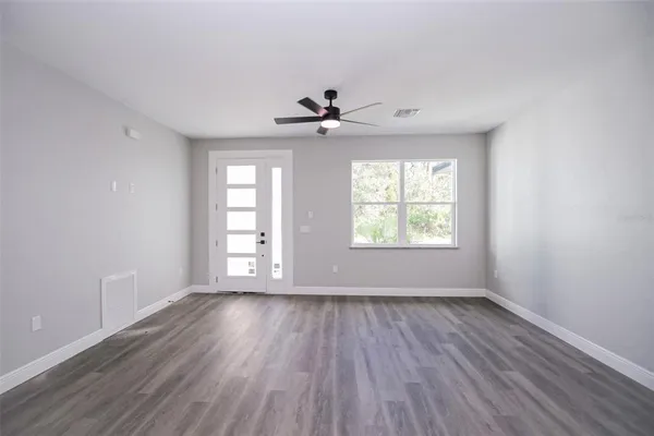 an empty room with wooden floor chandelier fan and windows