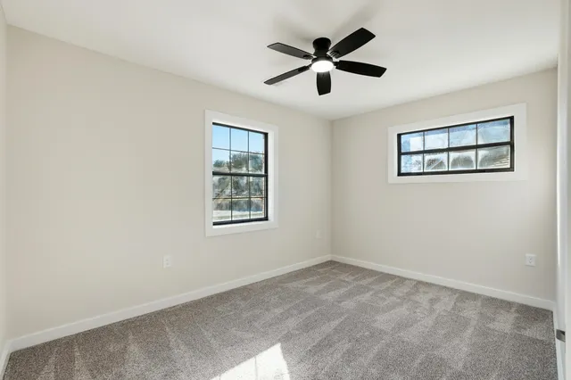 an empty room with ceiling fan and windows