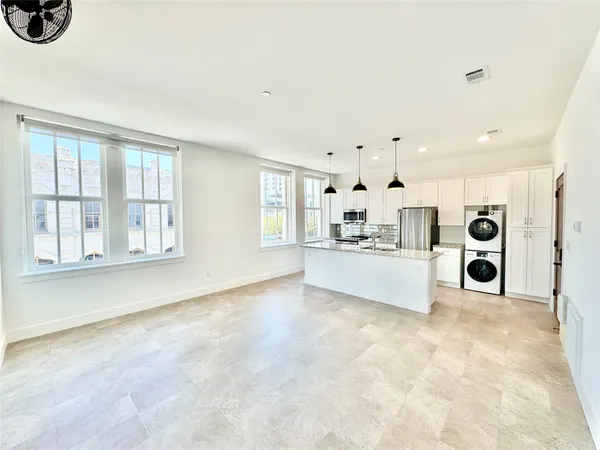 a view of an empty room with kitchen and window