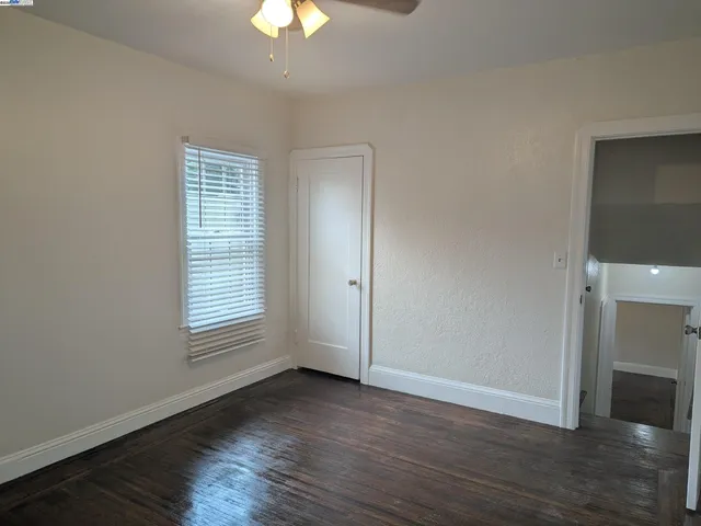 an empty room with wooden floor chandelier fan and windows