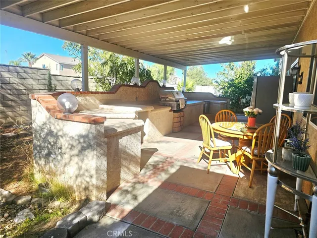 a view of a patio with table and chairs under an umbrella with a barbeque grill