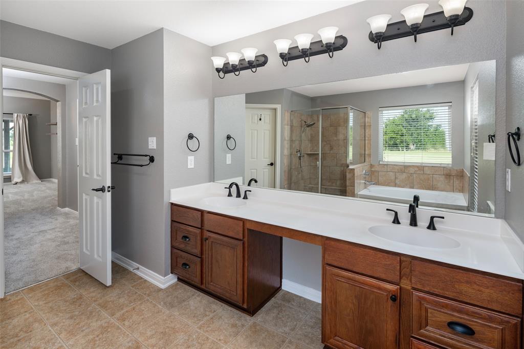 1019 Vaughan Lane Tioga, TX 76271 - Photo 24 of 40 Bathroom featuring a dual vanity with wood cabinetry and white countertops, a tiled walk-in shower with a glass enclosure, a built-in tub with tile surround, and a broad window