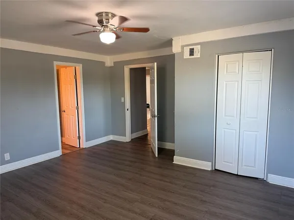a view of an empty room with wooden floor and a ceiling fan
