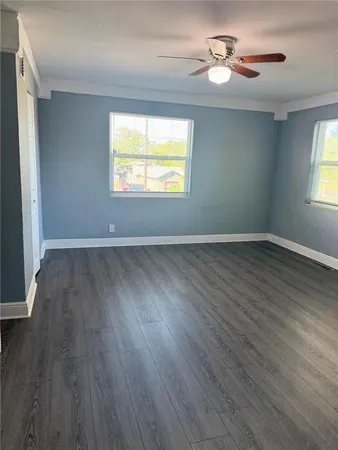 an empty room with wooden floor chandelier fan and windows