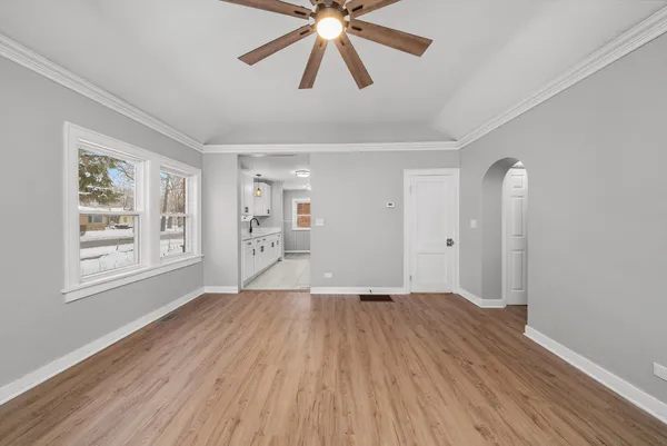 an empty room with wooden floor chandelier fan and windows