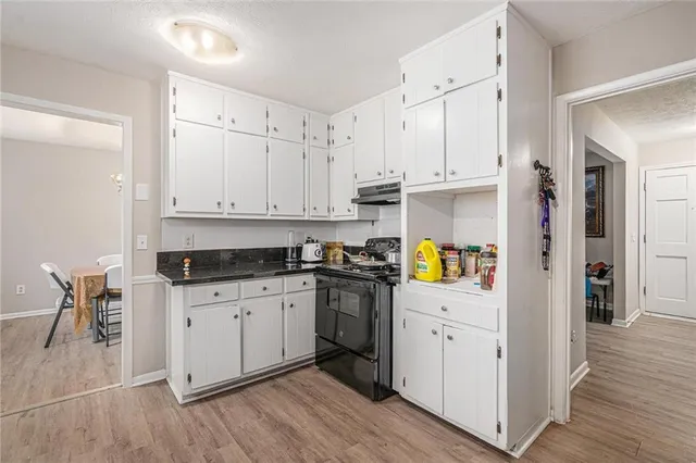 a kitchen with stainless steel appliances granite countertop a refrigerator a stove a sink and white cabinets with wooden floor