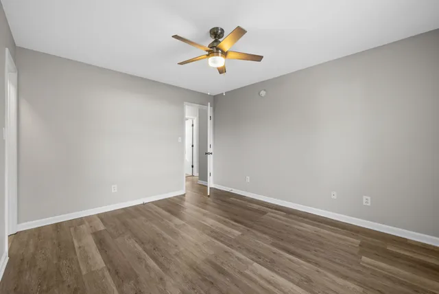 a view of an empty room with wooden floor and a ceiling fan