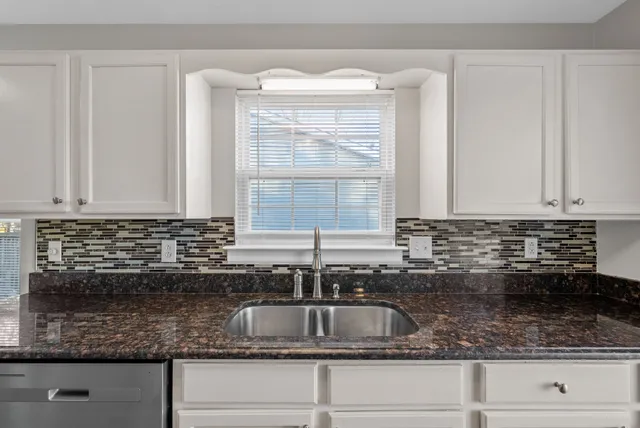 a kitchen with granite countertop a sink a window and cabinets