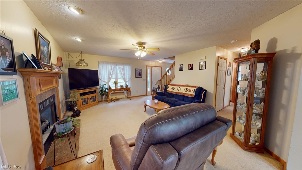 12431 Carter Road Painesville, OH 44077 - Photo 4 of 33 Living room featuring light colored carpet, a textured ceiling, ceiling fan, and a fireplace