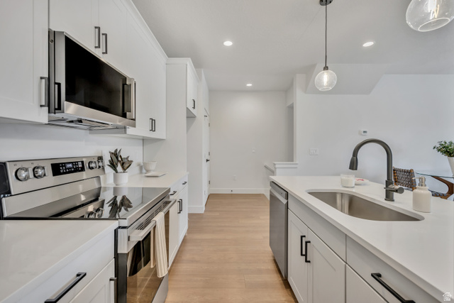 330 East 7635 S Street Sandy, UT 84047 - Photo 7 of 29 Kitchen with stainless steel appliances, white cabinets, light wood-type flooring, decorative light fixtures, and light stone countertops