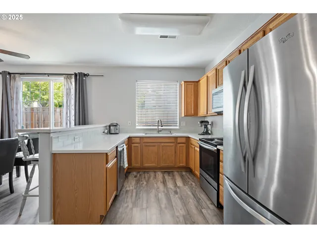 a kitchen with stainless steel appliances granite countertop a refrigerator a sink dishwasher a stove and white countertops with wooden floor