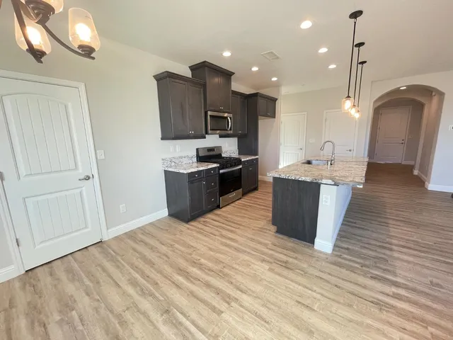a large room with kitchen island a sink wooden floor and stainless steel appliances