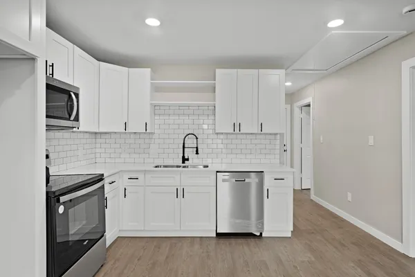 a kitchen with stainless steel appliances granite countertop a sink stove a refrigerator and white cabinets with wooden floor