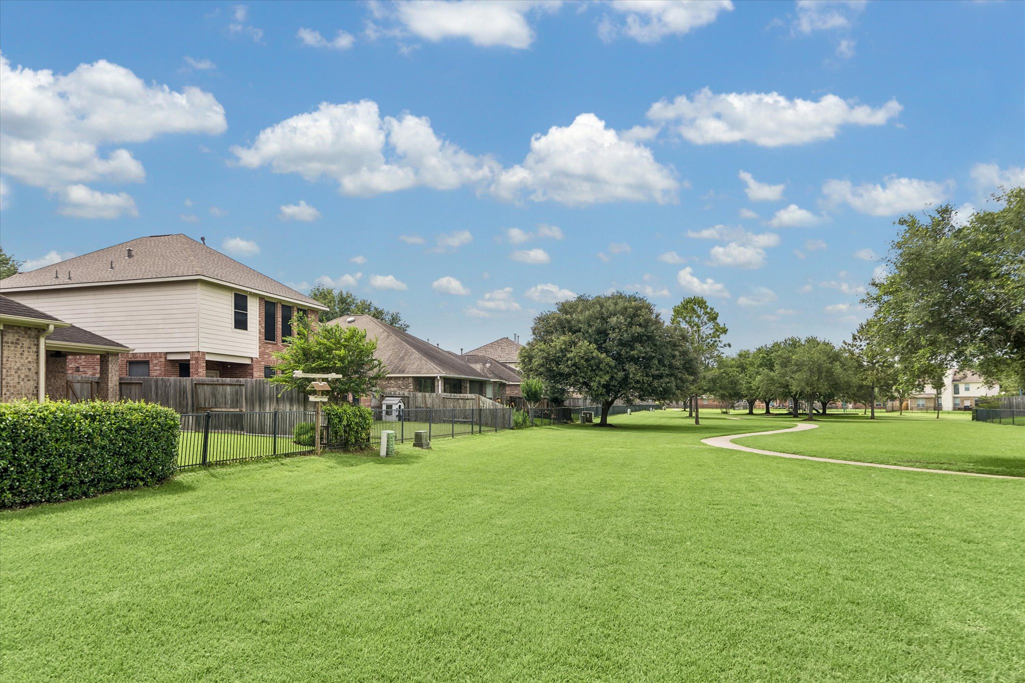 2214 Wembley Way Rosenberg, TX 77471 - Photo 18 of 35 Expansive green space featuring a winding paved pathway, mature trees, and a black wrought-iron fence bordering the property