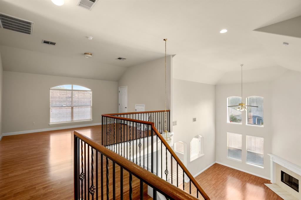 10105 Wind Cave Trail Austin, TX 78747 - Photo 14 of 23 Upper-level landing overlooking a lower living space, featuring wood-finish flooring, a wrought iron and wood banister, vaulted ceilings, and arched windows