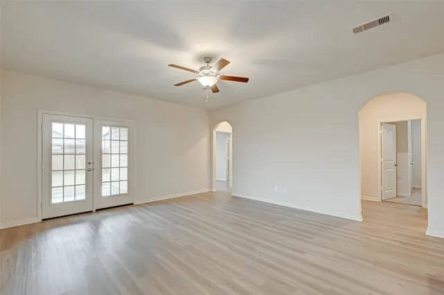 an empty room with wooden floor chandelier fan and windows