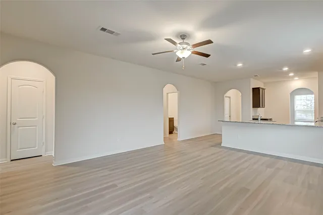 a view of an empty room with wooden floor and a ceiling fan