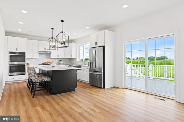 a kitchen with kitchen island stainless steel appliances a table chairs refrigerator and cabinets
