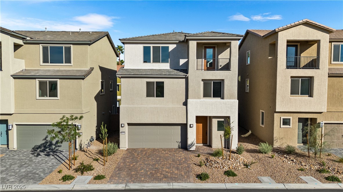 View of front of house with stucco siding, decorative driveway, an attached garage, and a residential view