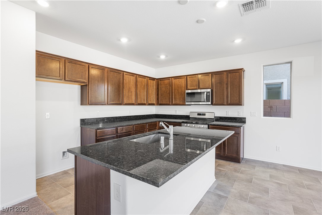 5670 Spring Trellis Street Las Vegas, NV 89113 - Photo 3 of 23 Kitchen with dark stone counters, appliances with stainless steel finishes, a center island with sink, recessed lighting, and brown cabinetry