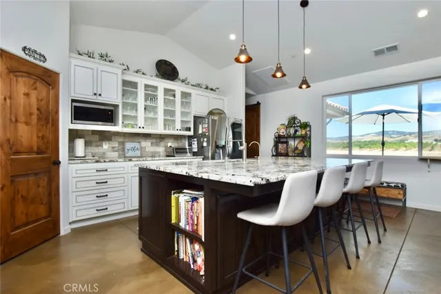 an open kitchen with granite countertop a stove a sink a dining table and chairs with wooden floor