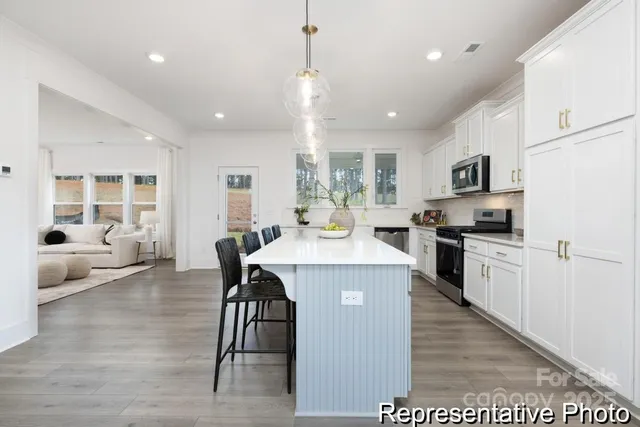 a kitchen with kitchen island granite countertop a stove a sink a refrigerator and white cabinets with wooden floor