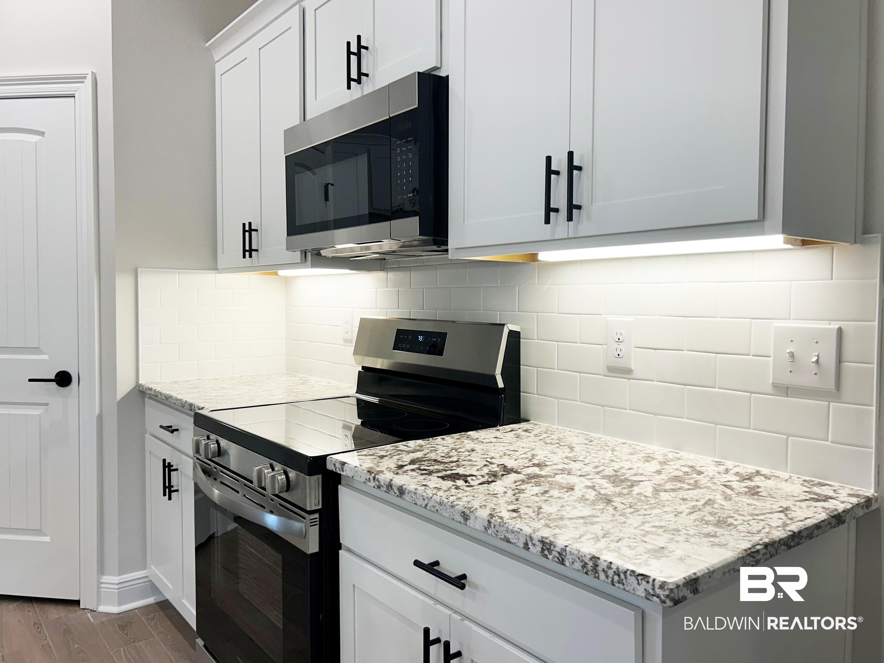 873 Sumter Loop Foley, AL 36535 - Photo 5 of 26 Kitchen with appliances with stainless steel finishes, white cabinetry, light stone counters, dark wood-style floors, and decorative backsplash