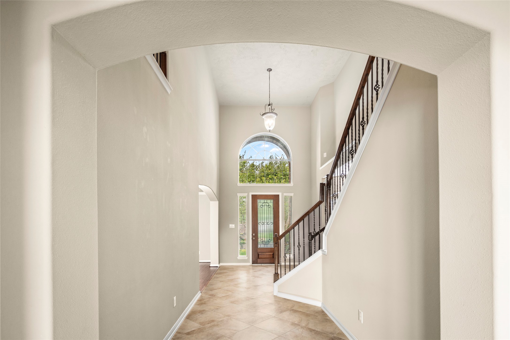 5307 Amber Sky Lane Rosharon, TX 77583 - Photo 5 of 50 Step into pure elegance: a dramatic two-story foyer crowned by a sweeping arched window, anchored by a graceful staircase finished in rich dark wood and wrought iron, set atop sun-kissed tile flooring.